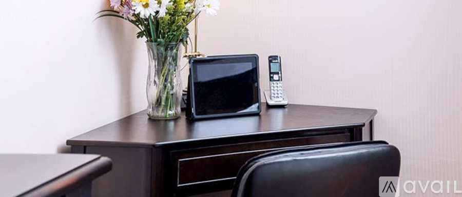 A black table with a vase of flowers, a cell phone, and a small TV on it.