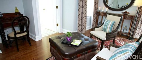 A living room with a brown leather ottoman and a chair with a striped pillow.