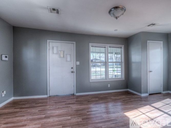 A room with grey walls and wooden flooring has two white doors and a window.