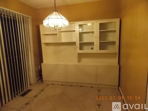 A room with a hanging light fixture and a cabinet with glass doors.