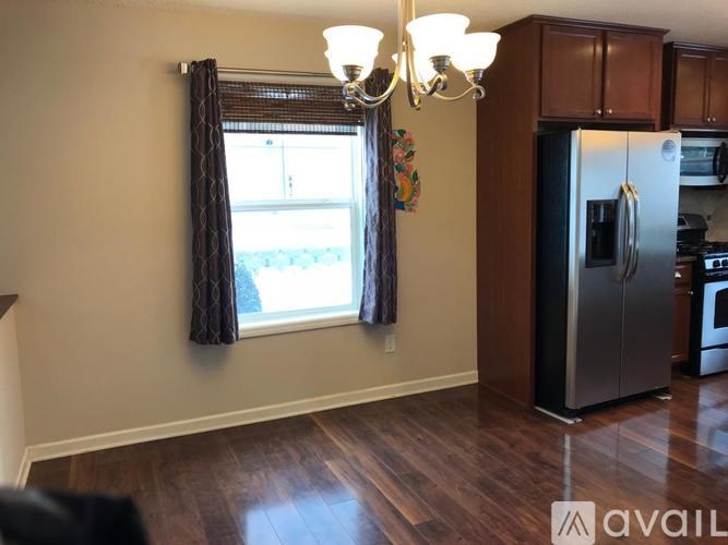 A kitchen with a refrigerator, cabinets, and a window with curtains.
