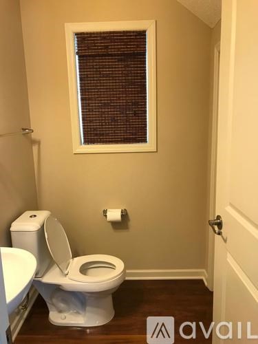 A white toilet in a bathroom with a window above it.