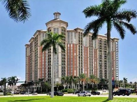 A large, multi-story building with a red and beige facade is surrounded by palm trees.