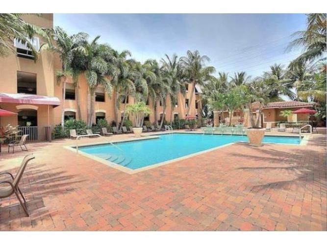 A pool surrounded by palm trees and a red brick patio.
