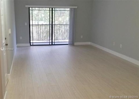 A spacious room with light wood flooring and a sliding glass door leading to a balcony.
