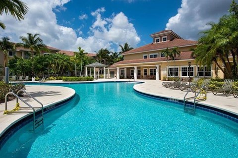 A large swimming pool in front of a building with palm trees around.