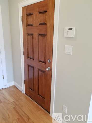 A wooden door in a room with a white wall and a light switch.