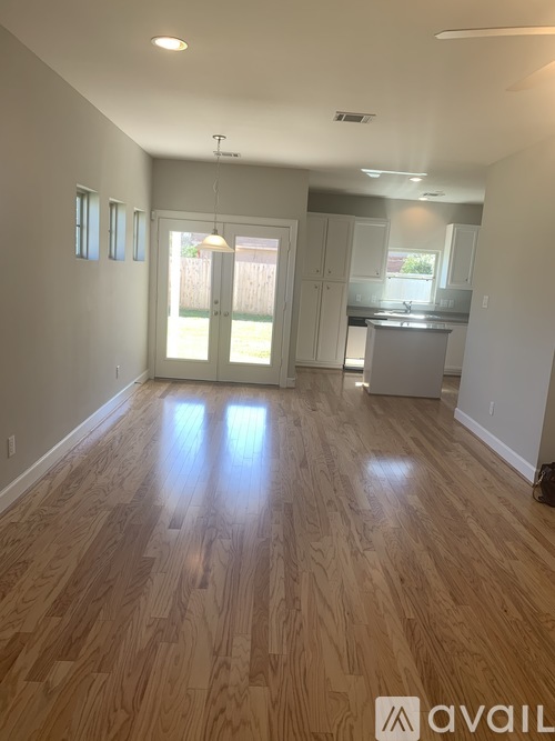 A spacious room with wooden flooring and a kitchen area in the background.