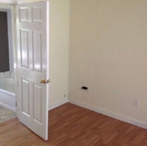 A white door with a gold handle is open to a room with wood flooring.