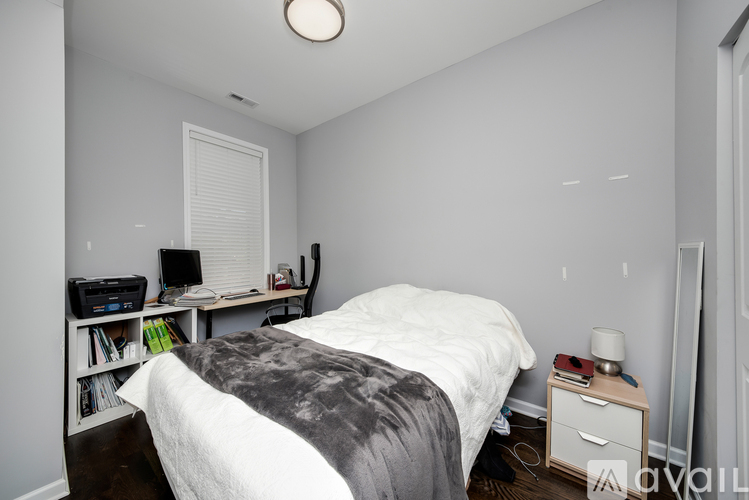 A bedroom with a bed, nightstand, and a desk with a lamp.