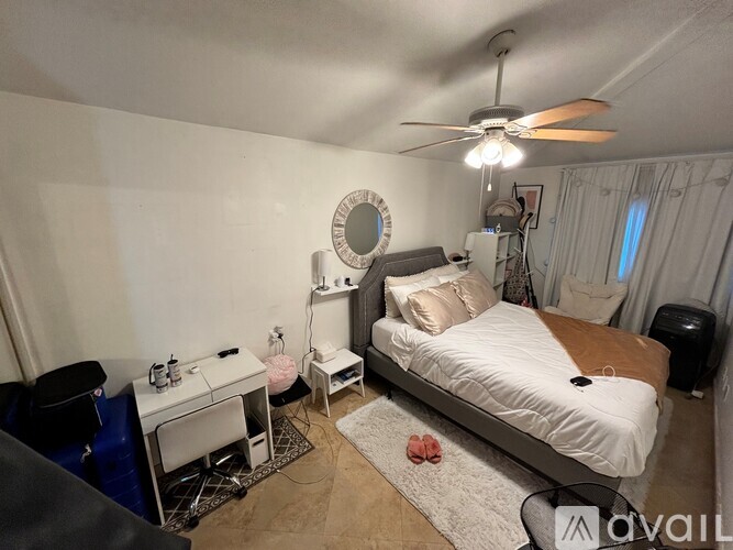 A bedroom with a bed, a desk, a chair, a fan, and a rug.
