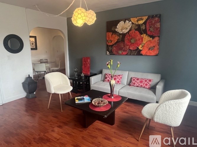 A living room with a grey couch, a white chair, a coffee table, and a painting on the wall.