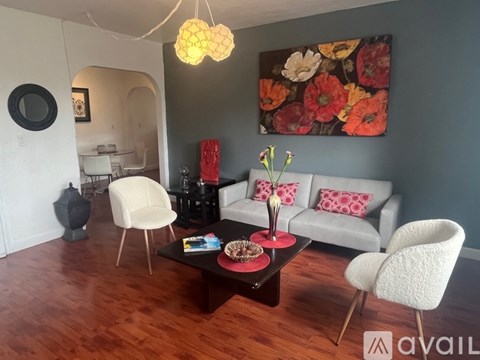 A living room with a grey couch, a white chair, a coffee table, and a painting on the wall.
