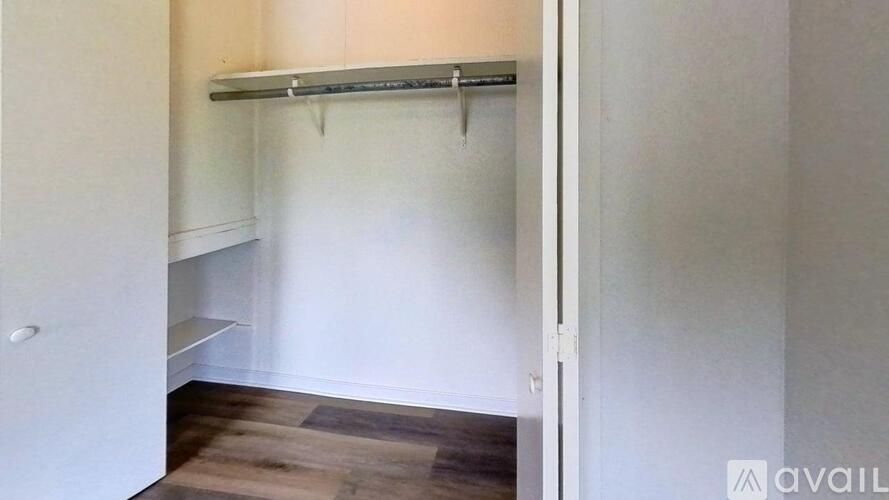 A room with wooden floors and a kitchen area in the background.