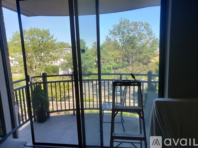 A balcony with a chair and a table with a view of trees and a street.