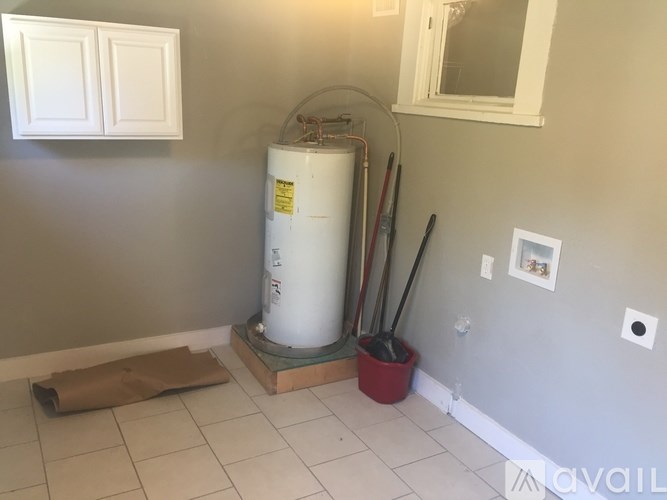 A room with a water heater and a broom.