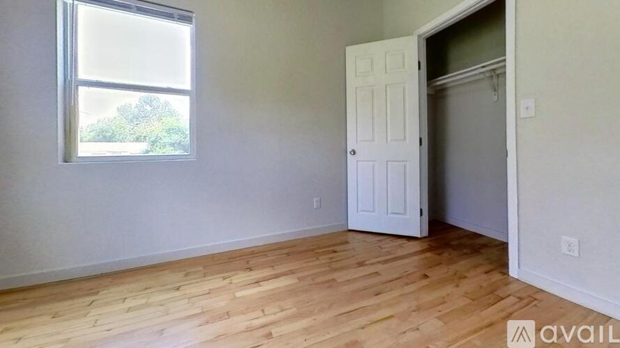 A room with a white door and a window with a view of trees outside.