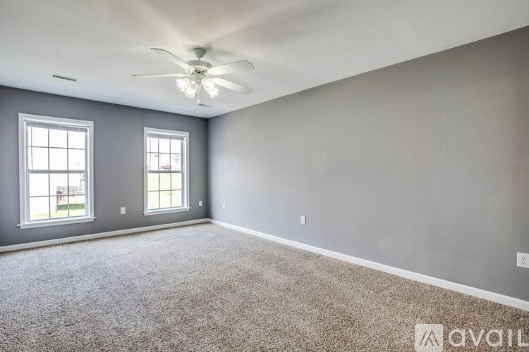 A spacious room with a ceiling fan and two windows.