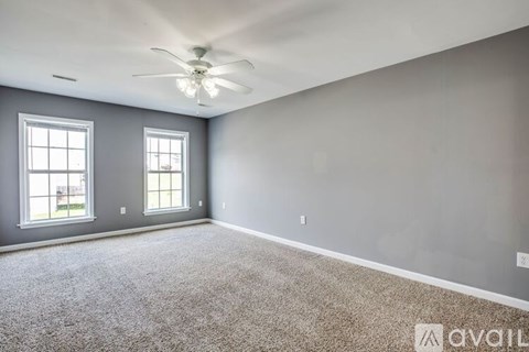 A spacious room with a ceiling fan and two windows.