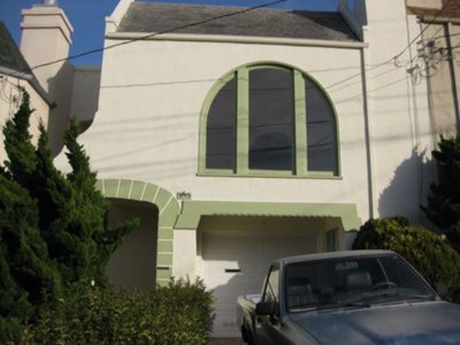 A car is parked in front of a white house with a green arched window.