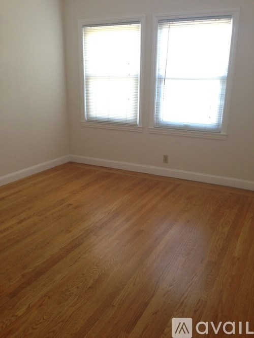 A room with wooden flooring and two windows.