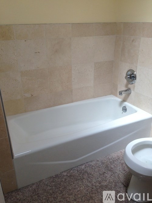A white bathtub is in a bathroom with tile walls.