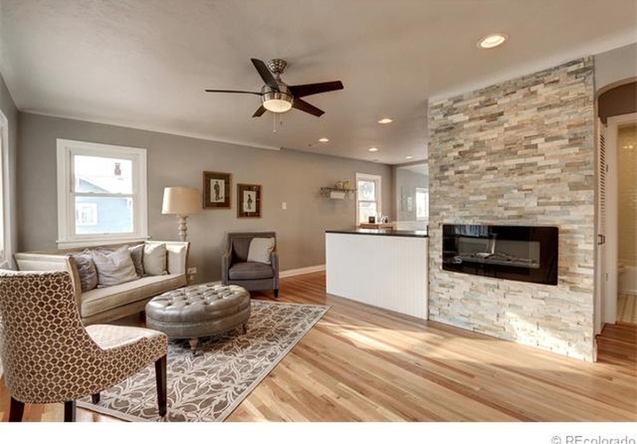 A living room with a stone fireplace and a ceiling fan.