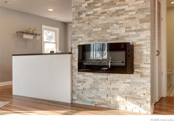 A stone fireplace with a black grate in a room with a wooden floor.