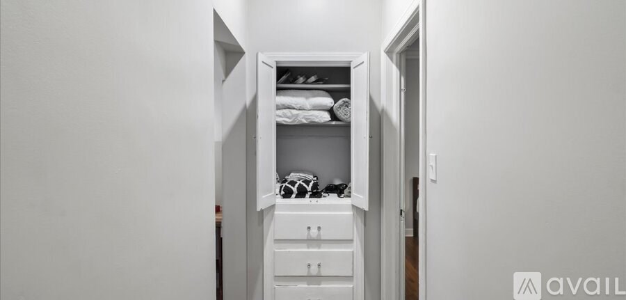 A white closet with clothes and a shelf.