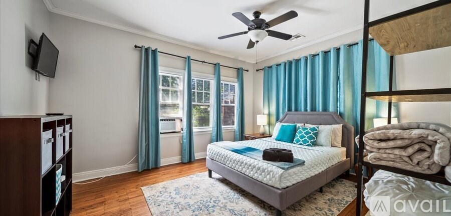 A bedroom with a bed, a ceiling fan, and a window with blue curtains.