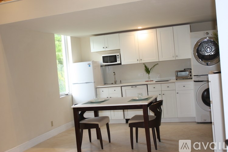 A kitchen with white cabinets and appliances, a table with two chairs, and a window letting in natural light.
