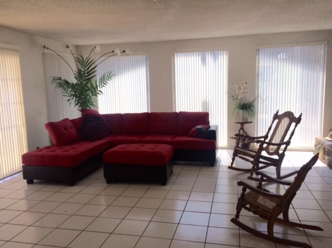 A red couch with a bench in front of it and a rocking chair to the side.