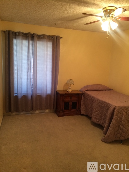 A bedroom with a bed, nightstand, and window with curtains.