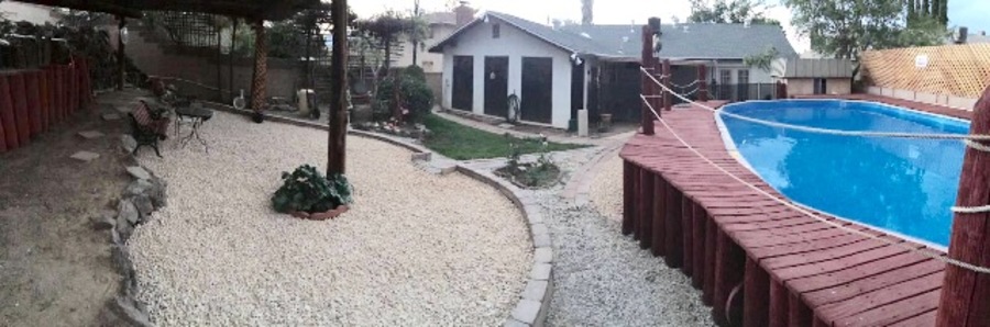 A pool with a wooden deck and a gravel area with a house in the background.