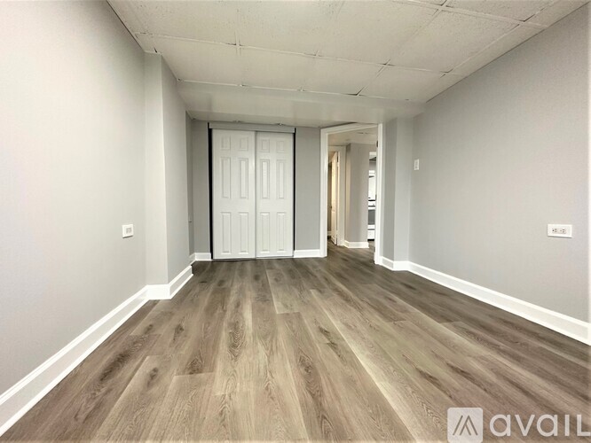 A room with wooden flooring and white walls, with a door in the middle.