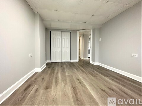 A room with wooden flooring and white walls, with a door in the middle.