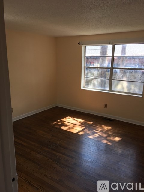 A room with wooden flooring and a window letting in sunlight.