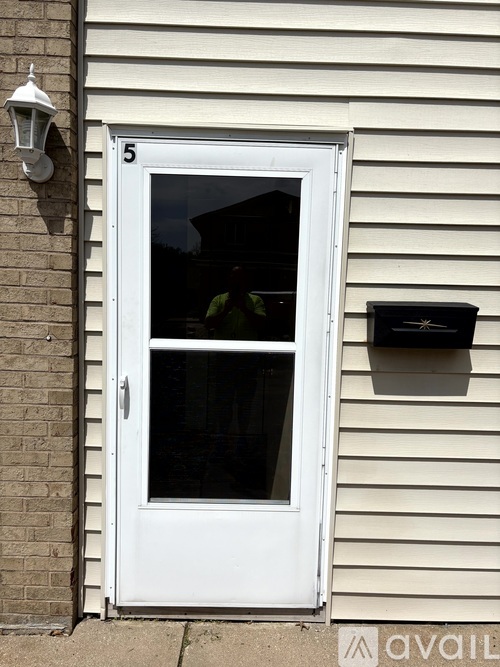 A white door with a glass window and a mailbox on the siding of a house.