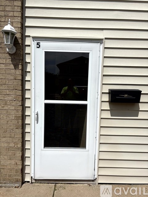 A white door with a glass window and a mailbox on the siding of a house.