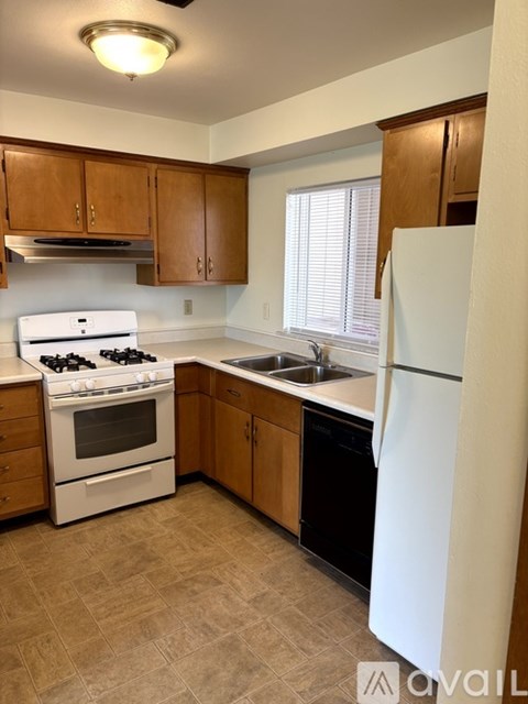 A kitchen with a white stove top oven, white refrigerator, and brown cabinets.