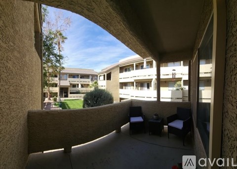 A balcony with chairs and a table is seen through a window.