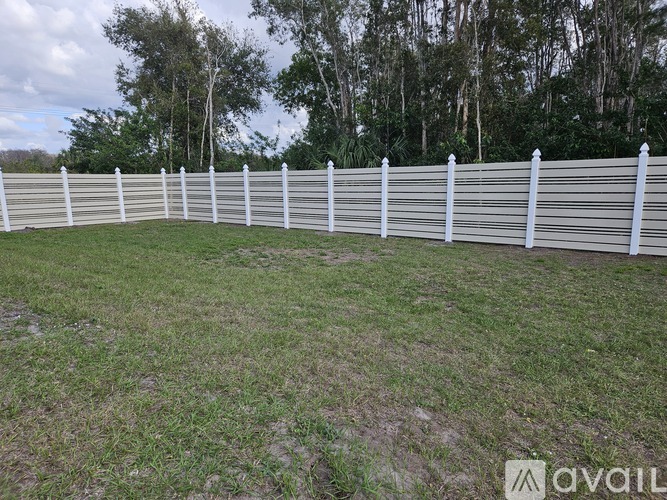 A white fence encloses a grassy area with trees in the background.