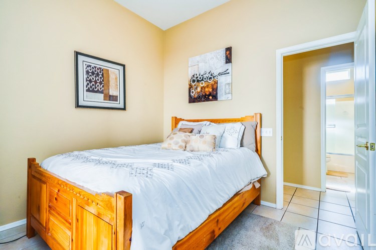 A bedroom with a bed, two pictures on the wall, and a doorway leading to another room.