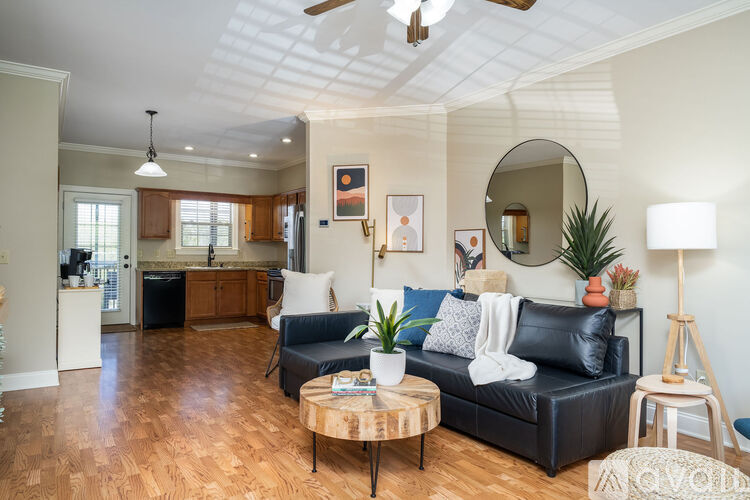 A living room with a black leather couch and a round mirror on the wall.