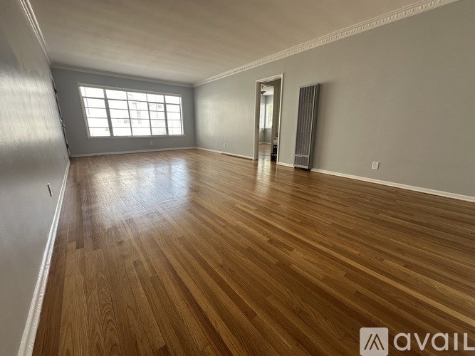 A spacious room with wooden flooring and a large window.