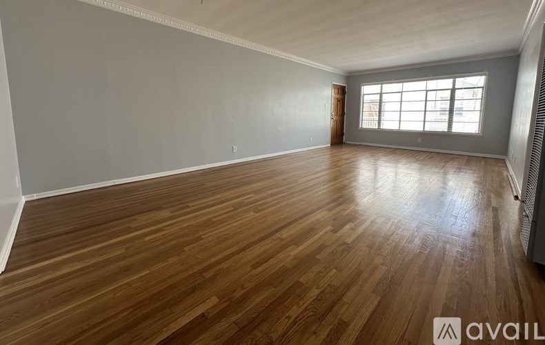 A spacious room with wooden flooring and a large window.