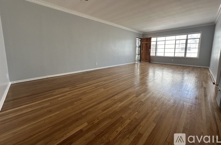A spacious room with wooden flooring and a large window.