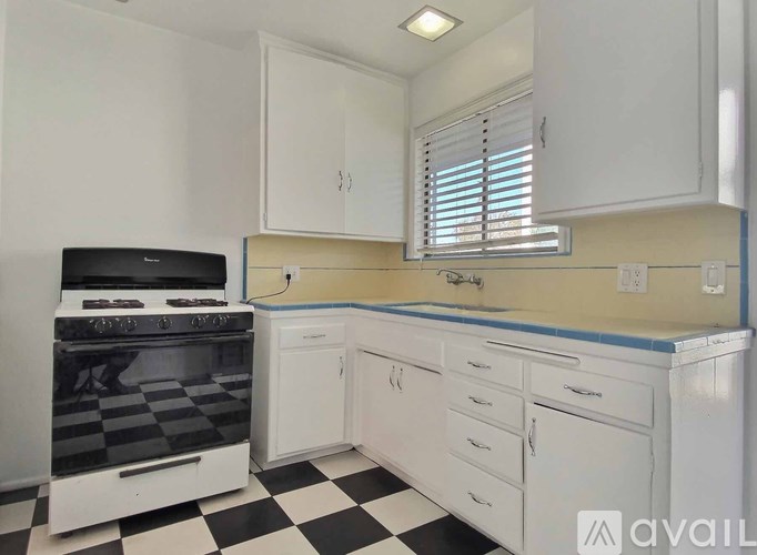 A black and white checkered floor in a kitchen with white cabinets and a black stove top.