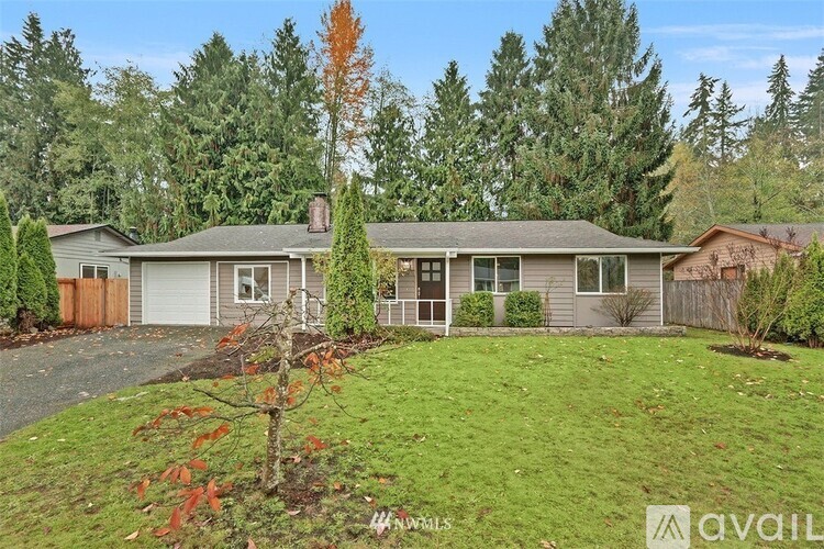 A house with a grey roof and a white garage door is surrounded by trees.