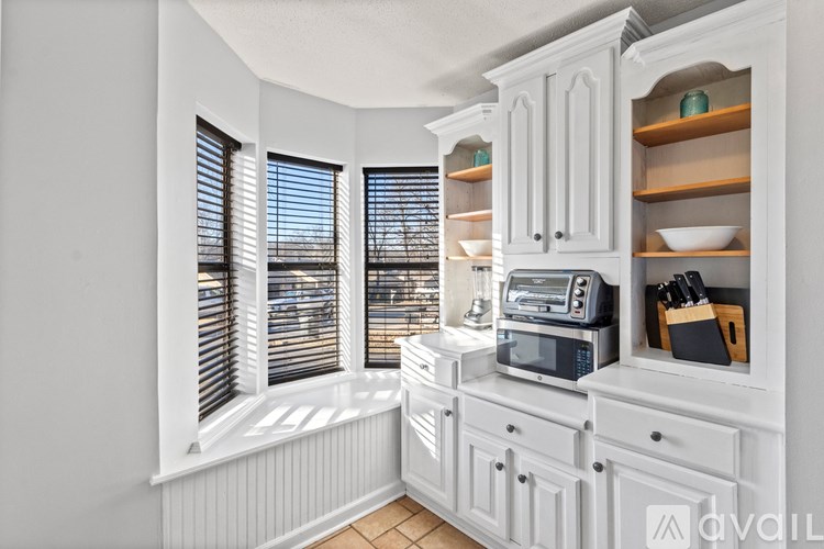 A kitchen with white cabinets and a window with blinds.